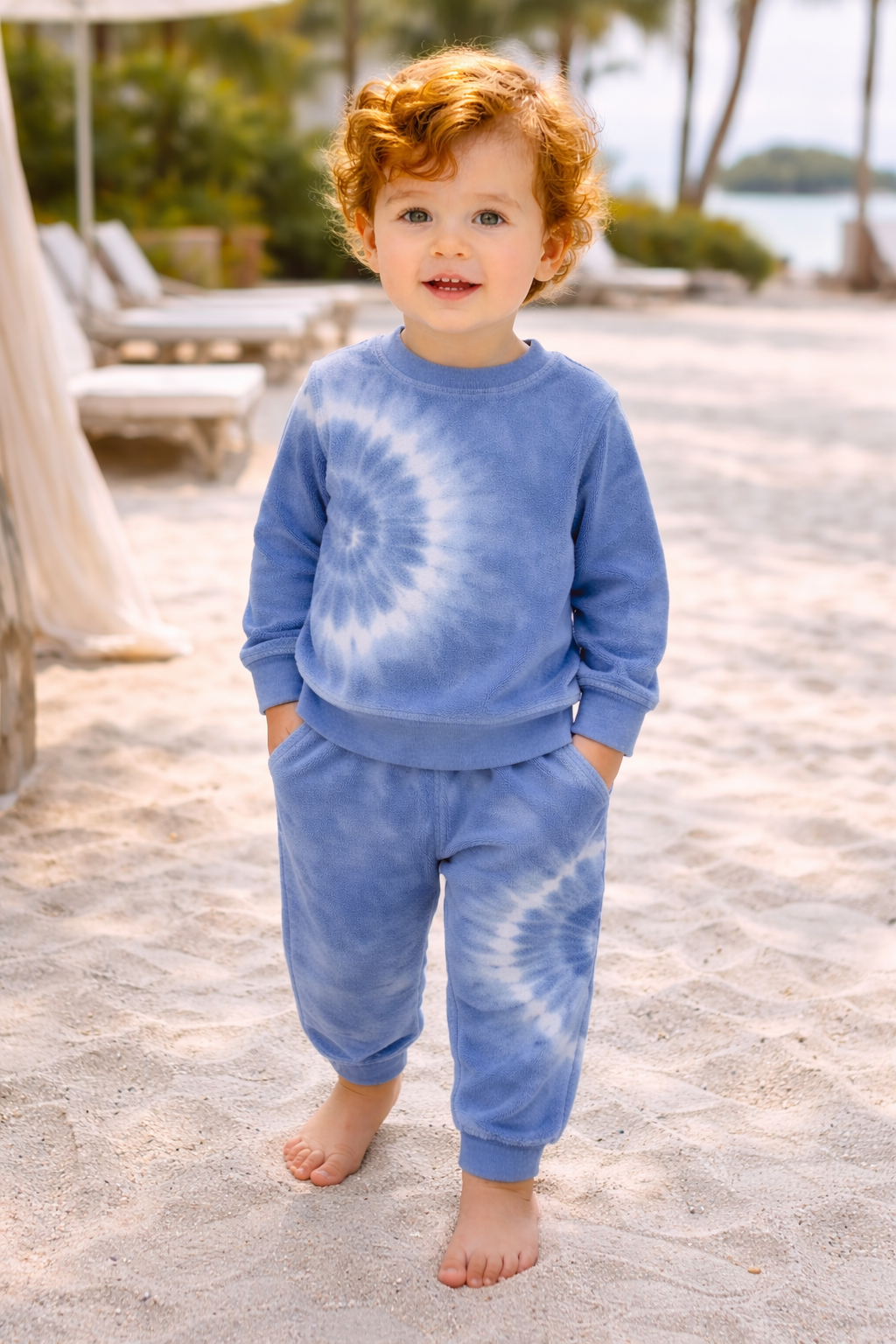 Child wearing a blue tie-dye outfit standing on a sandy beach.
