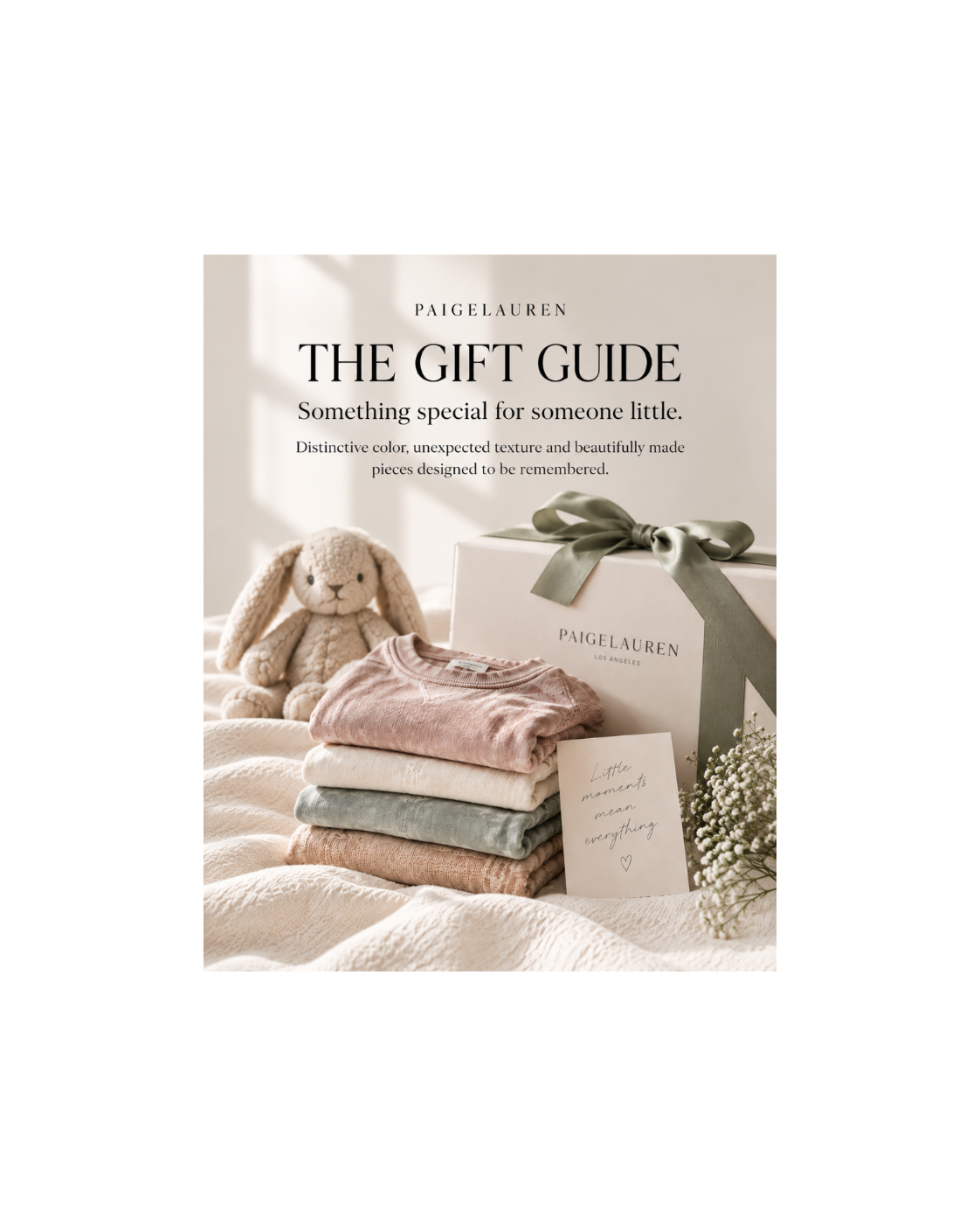 A styled gift set from Paigelauren on a soft cream fabric backdrop, featuring a white branded gift box tied with a sage ribbon, folded pastel textiles, a plush bunny toy, and a small card. Large text at the top reads 'THE GIFT GUIDE' with Paigelauren branding.