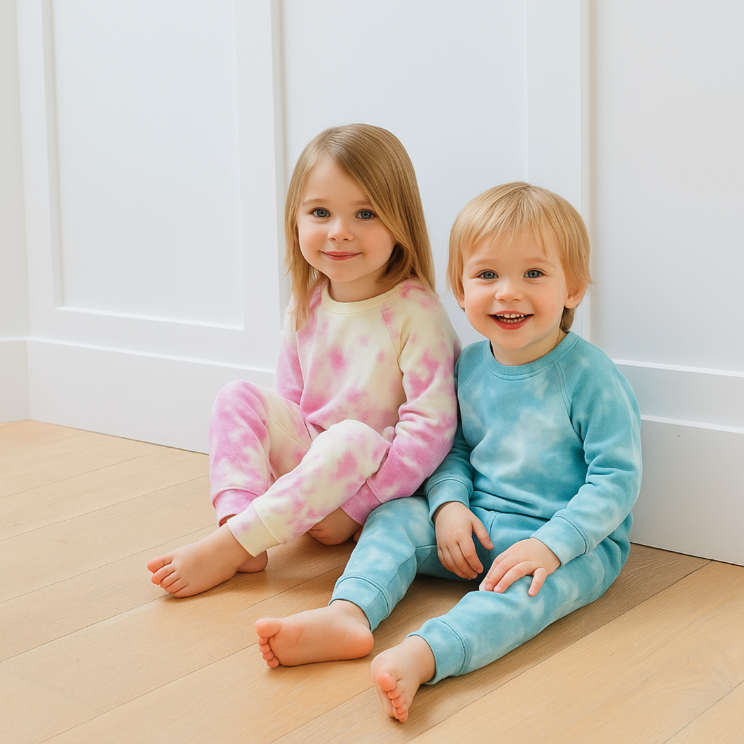 Two children sitting on a wooden floor wearing tie-dye pajamas.