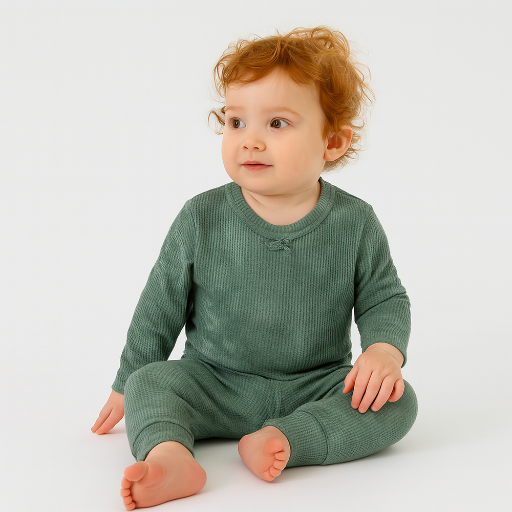 Baby wearing a green outfit sitting on a white background
