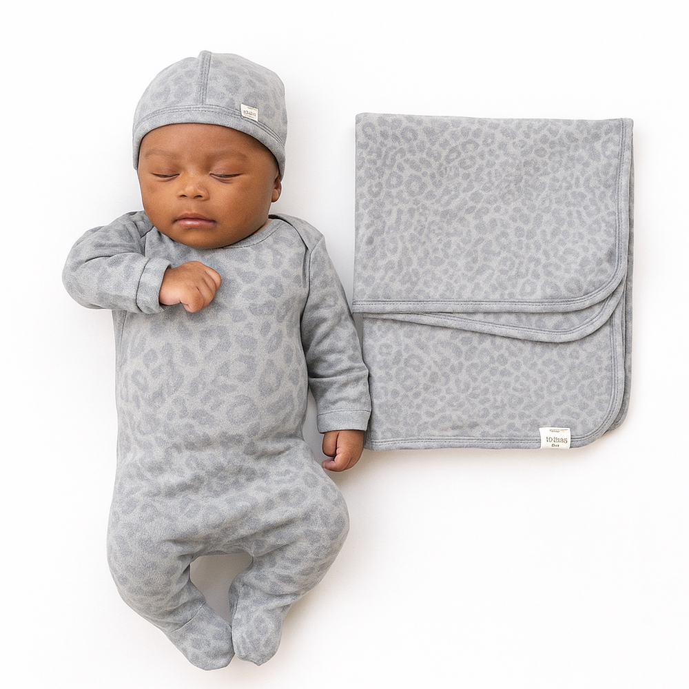 Baby in gray leopard print outfit with matching blanket on a white background