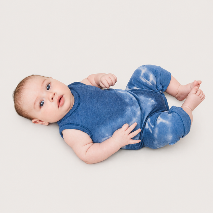 Baby lying down wearing the PAIGELAUREN Blue Baby Rib Tie Dye Tank Overall