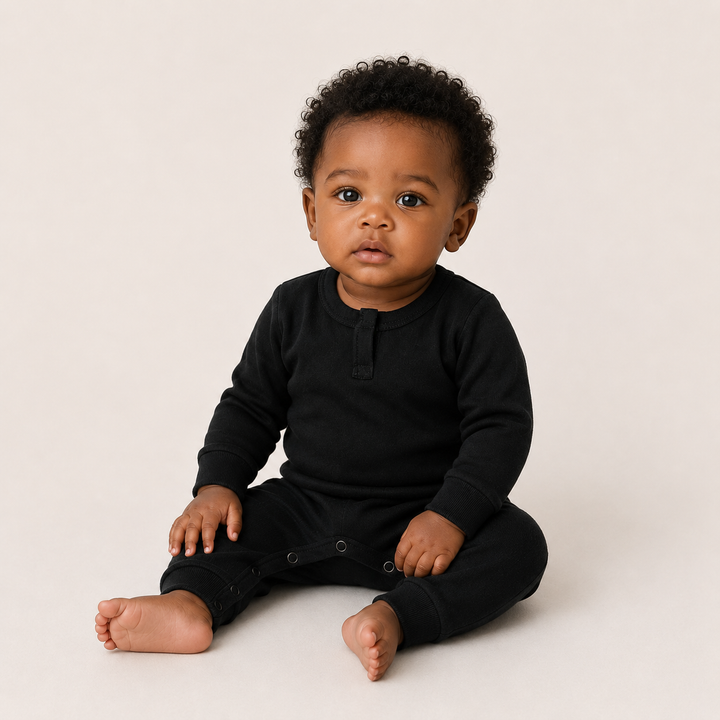 Baby wearing the PAIGELAUREN Fleece Sweatshirt Henley Romper in black while sitting