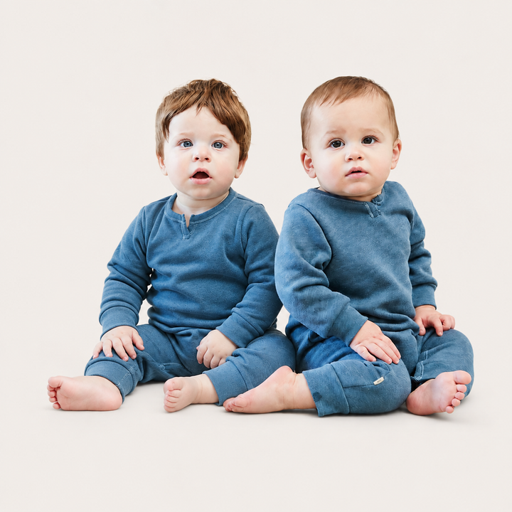 Two Babies wearing the PAIGELAUREN Fleece Sweatshirt Henley Romper in Dusty Blue while sitting