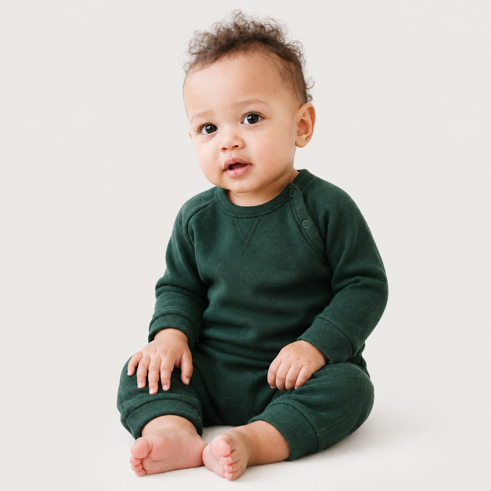 Baby wearing the PAIGELAUREN Fleece Sweatshirt Raglan Romper in dark green while sitting