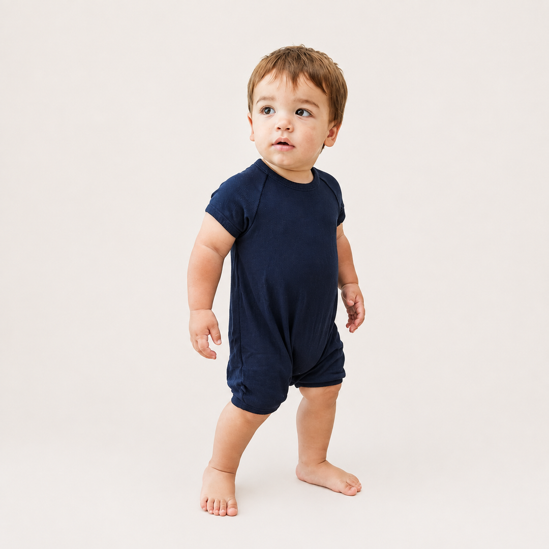 baby standing while wearing the PAIGELAUREN Garment Dye Ribbed Shortall Onesie. navy