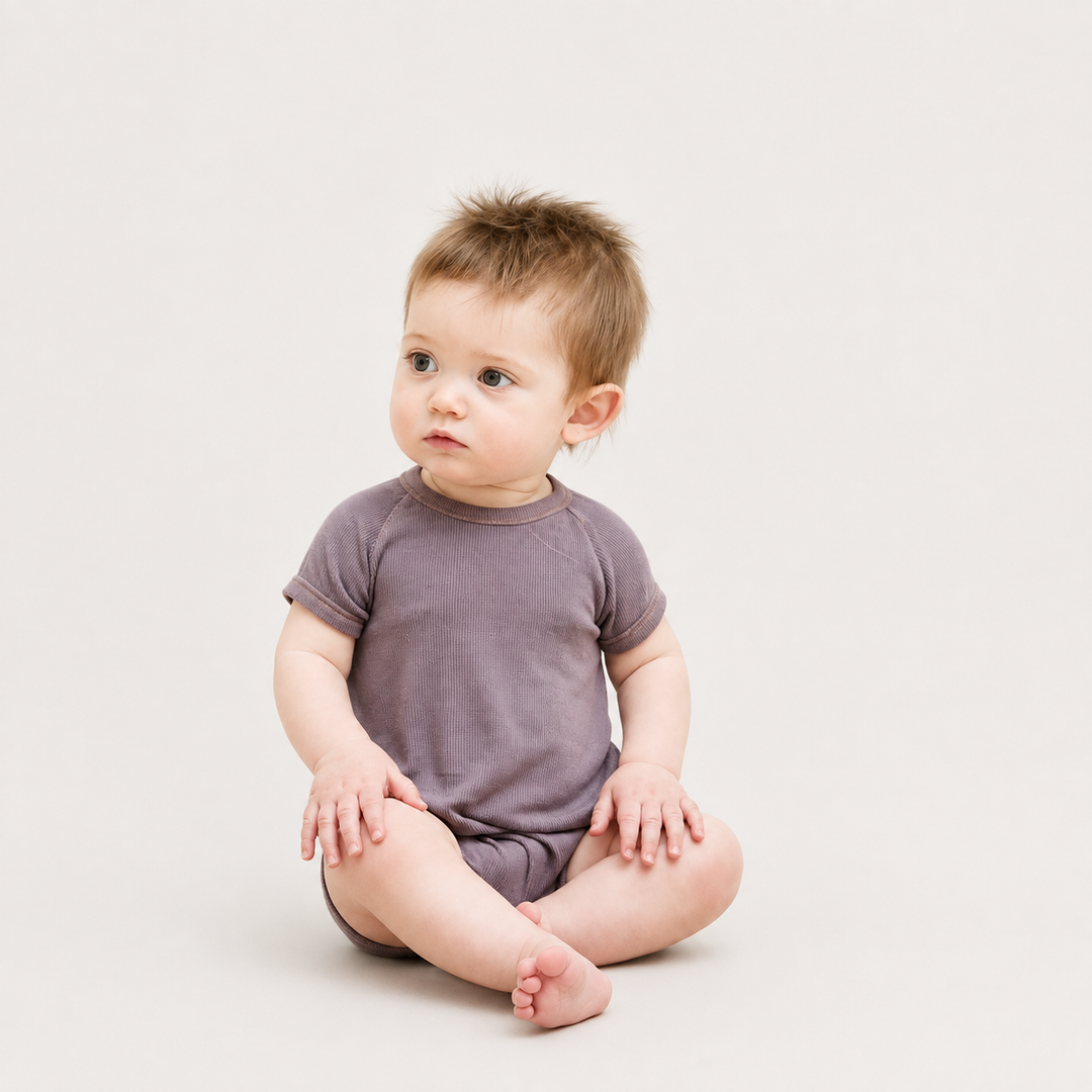 Baby wearing the PAIGELAUREN Garment Dye Ribbed Shortall Onesie in Plum while sitting