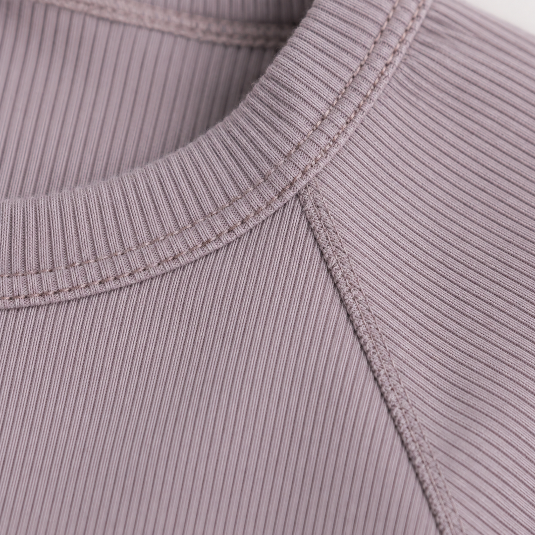 Close-up of the ribbed crew neckline and raglan shoulder construction on the PAIGELAUREN Garment Dye Ribbed Shortall Onesie. Plum