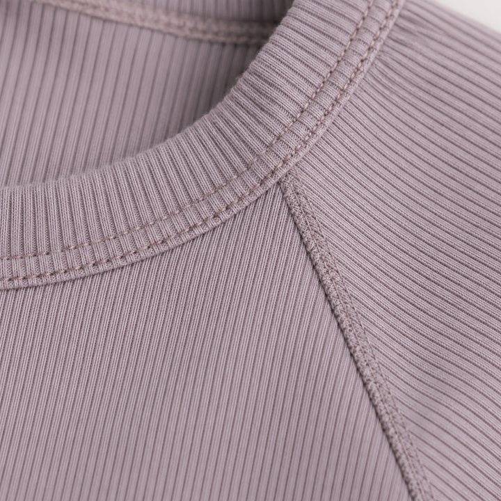 Close-up of the ribbed crew neckline and raglan shoulder construction on the PAIGELAUREN Garment Dye Ribbed Shortall Onesie. Plum