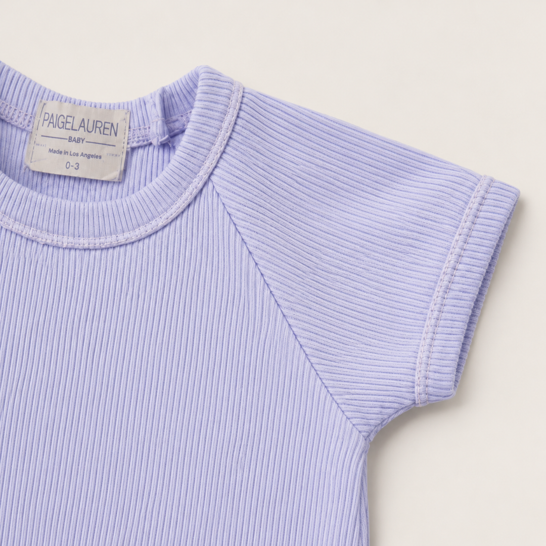 Detail of the raglan sleeve, cuff, and premium rib knit on the PAIGELAUREN Garment Dye Ribbed Shortall Onesie. Lavender