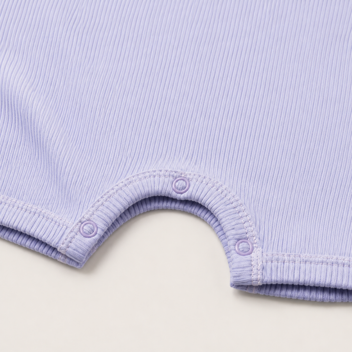 Close-up of the color-matched ring snap closure and reinforced inseam on the PAIGELAUREN Garment Dye Ribbed Shortall Onesie. Lavender
