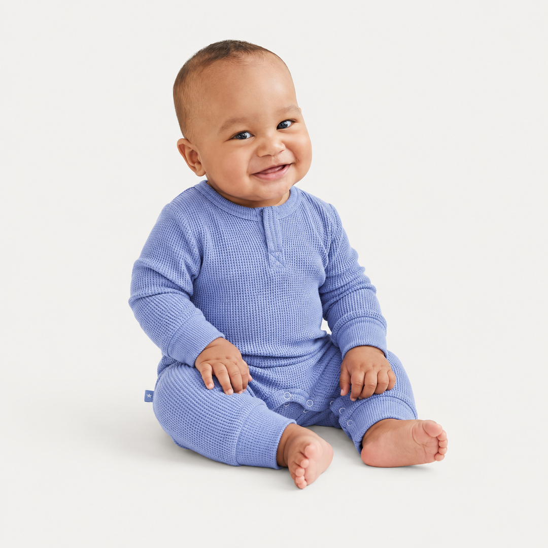 Baby wearing the PAIGELAUREN Garment Dyed Thermal Romper in blue while sitting in a bright studio