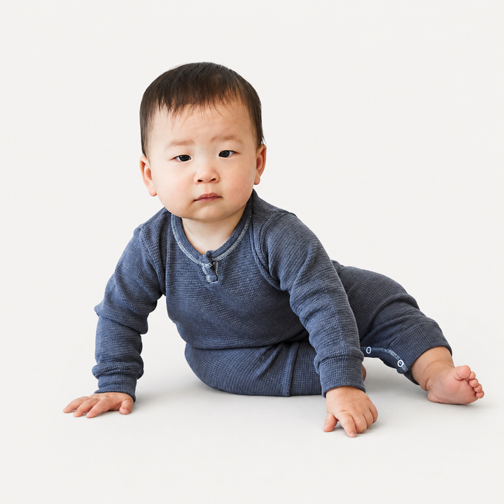 Baby wearing the PAIGELAUREN Garment Dyed Thermal Romper in gray while sitting in a bright studio