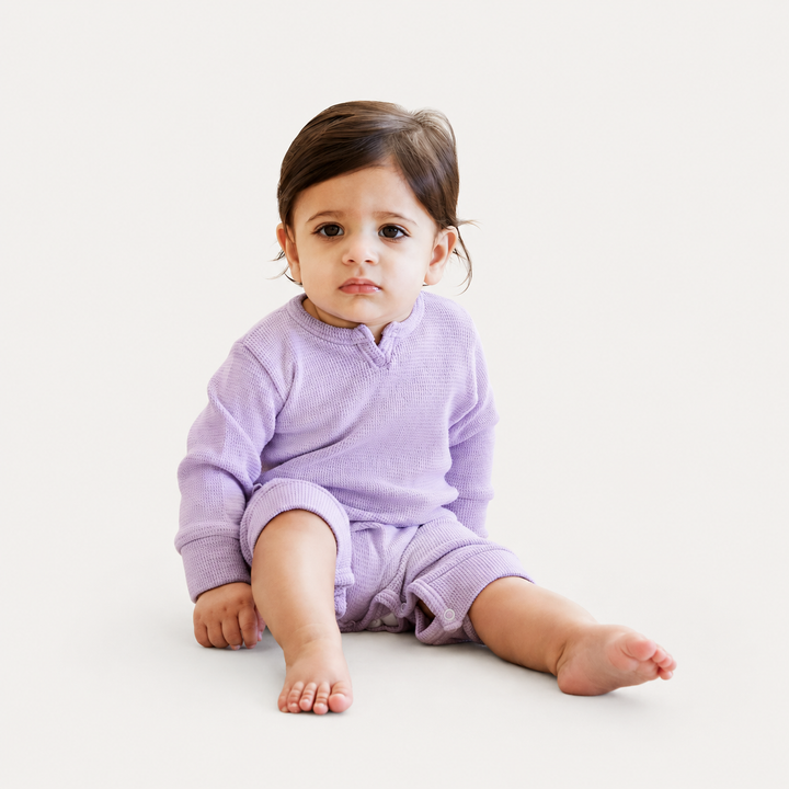 Baby wearing the PAIGELAUREN Garment Dyed Thermal Romper in lilac while sitting in a bright studio