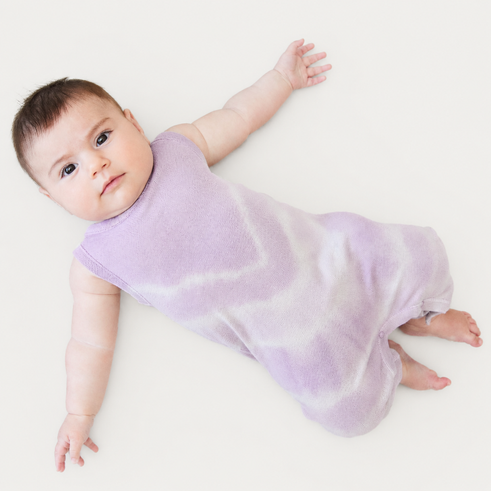 Baby lying down wearing the PAIGELAUREN Lavender Baby Rib Tie Dye Tank Overall