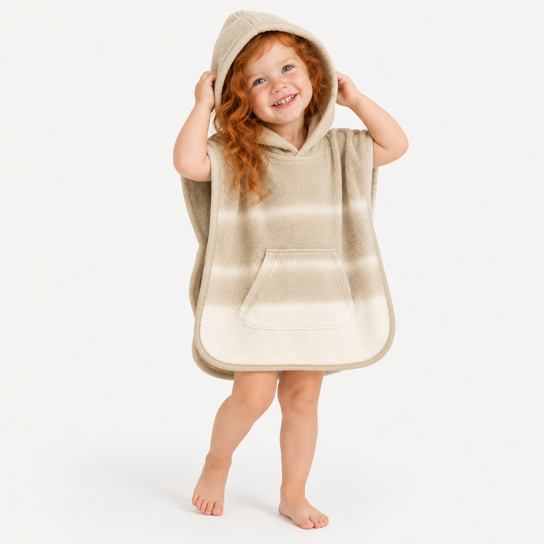 Red-haired toddler girl smiling with hood up in beige ombré terry poncho