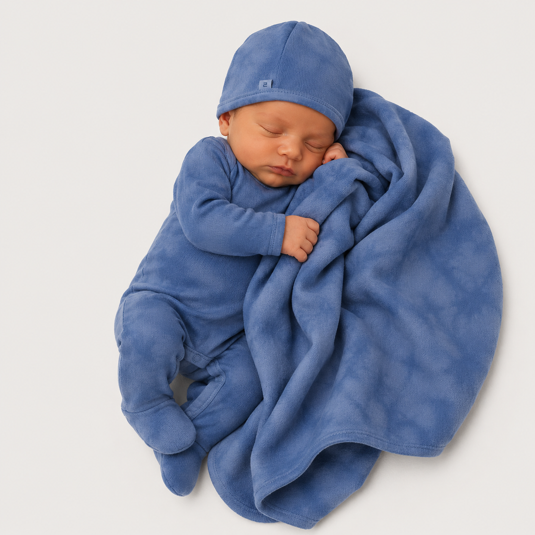 Newborn wearing Blue Marble Brushed Hacci romper and beanie while snuggling with matching blanket