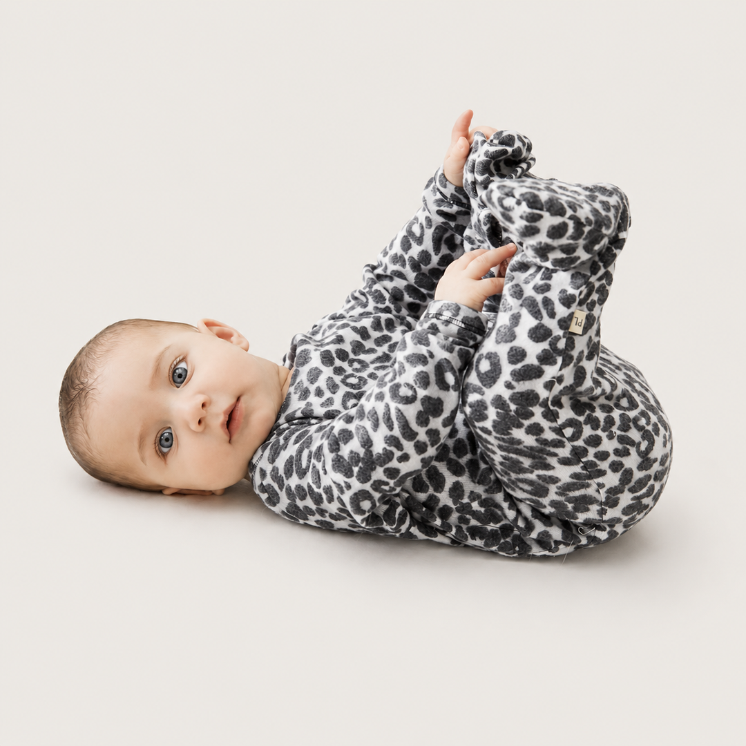 Baby lying down in PAIGELAUREN black and white animal print Brushed Hacci Footed Pajama