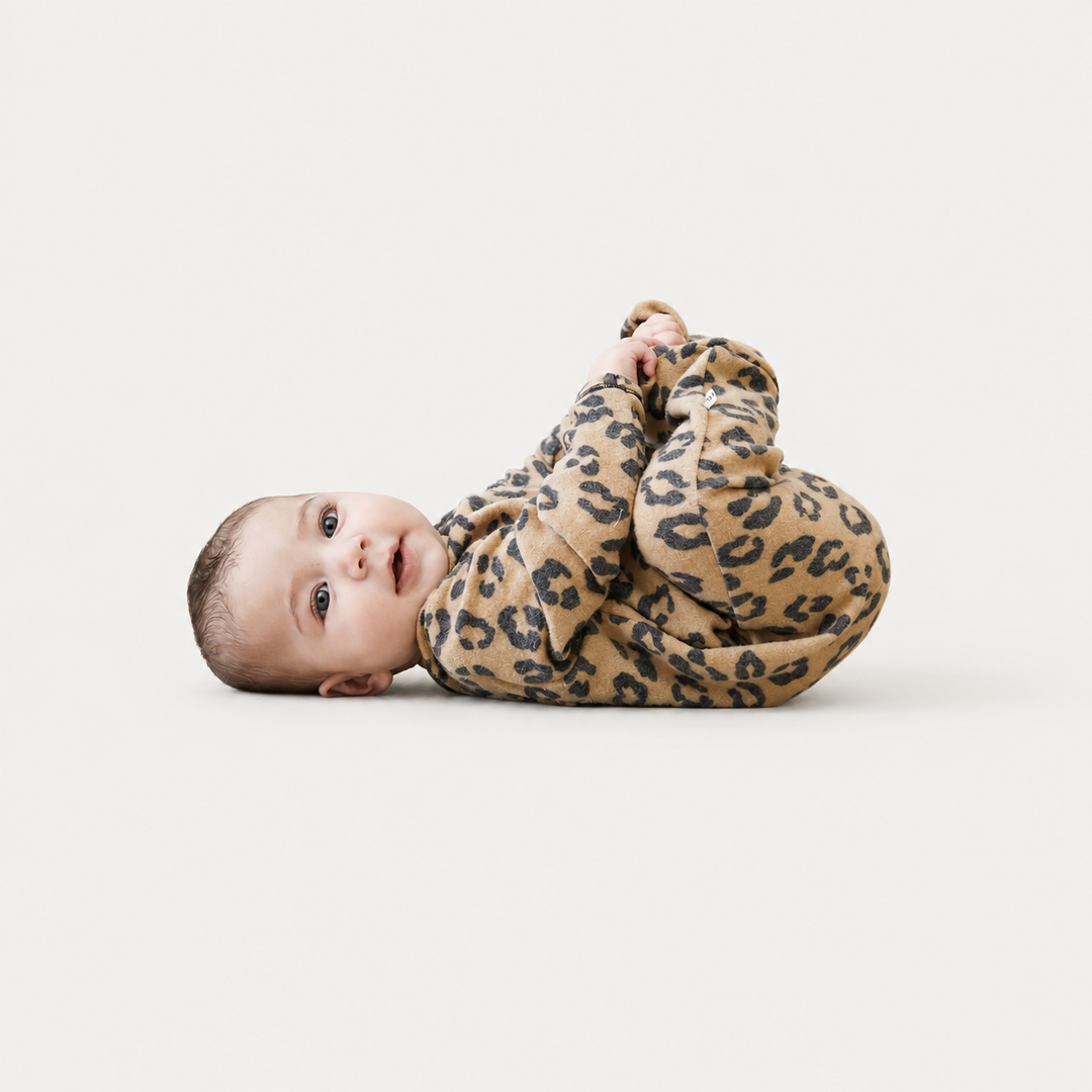 Baby lying down wearing the PAIGELAUREN camel animal print Brushed Hacci Footed Pajama