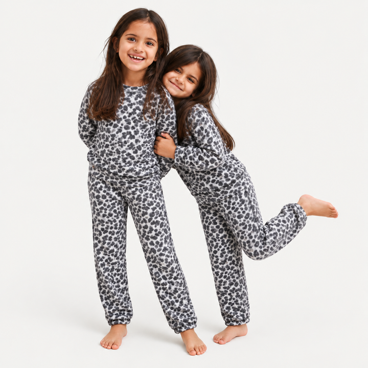 Two young girls wearing matching white and black leopard-print pajama sets, posing together against a clean white studio background.