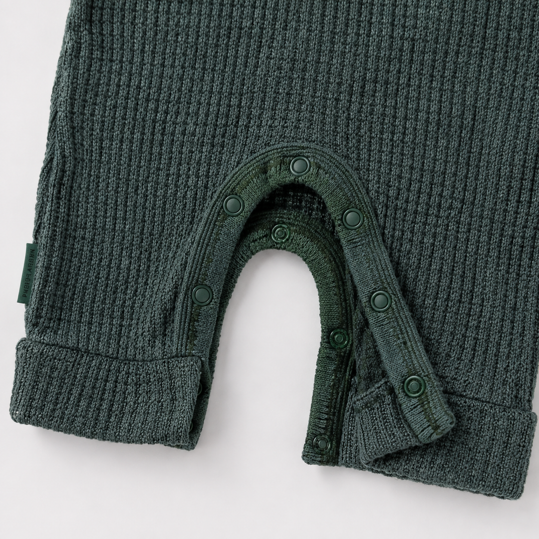Close-up of a dark green ribbed knit baby garment, likely a footless one-piece or bodysuit, showing the leg opening with snap closures and ribbed cuffs on a white background.