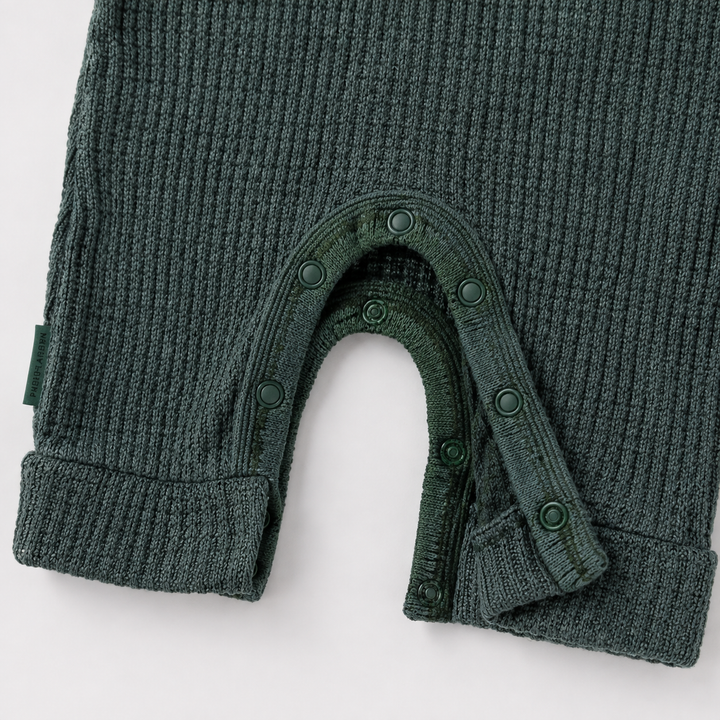 Close-up of a dark green ribbed knit baby garment, likely a footless one-piece or bodysuit, showing the leg opening with snap closures and ribbed cuffs on a white background.