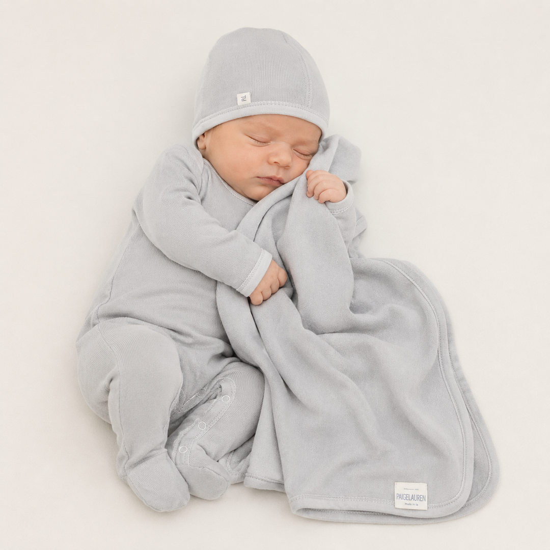 Newborn wearing PAIGELAUREN Gray Fleece romper and beanie while snuggling with matching baby blanket