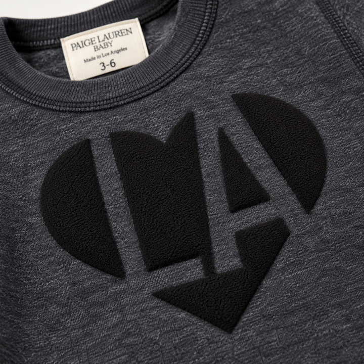 Close-up of black puffed LA heart graphic on PAIGELAUREN Heathered Black fleece