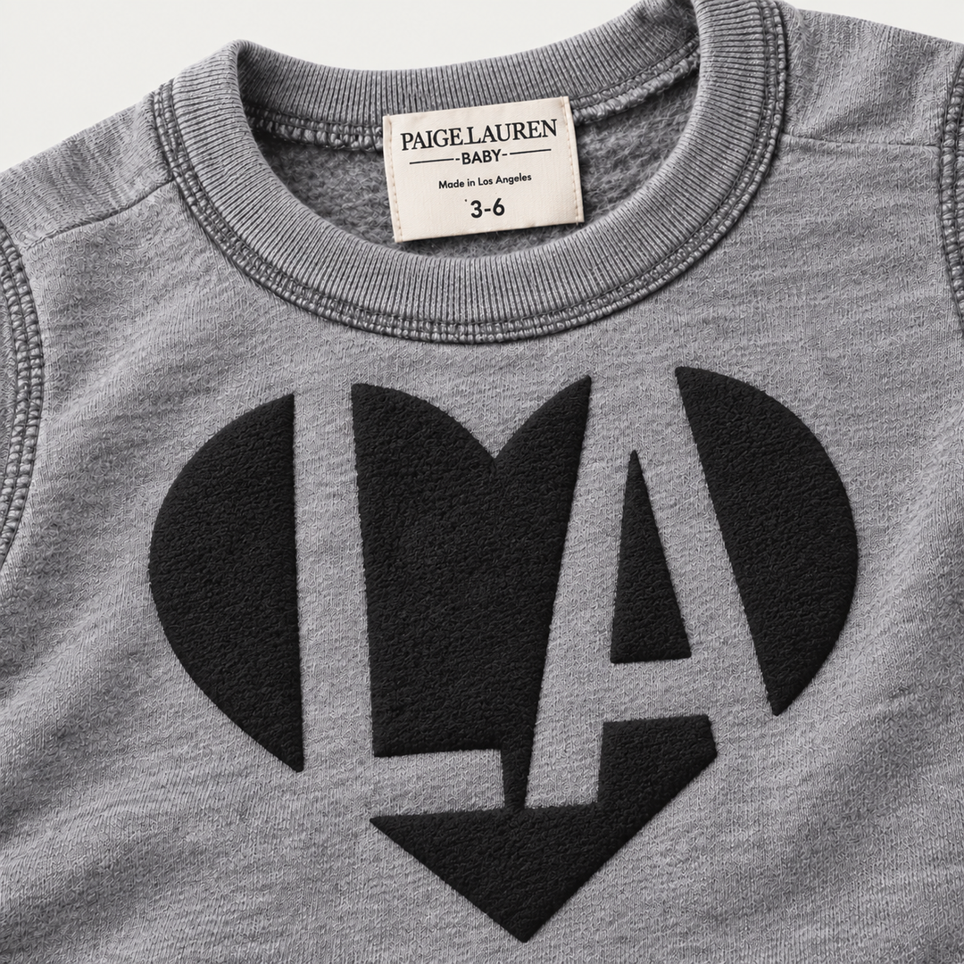 Close-up of black puffed LA heart graphic on PAIGELAUREN Heathered Gray fleece