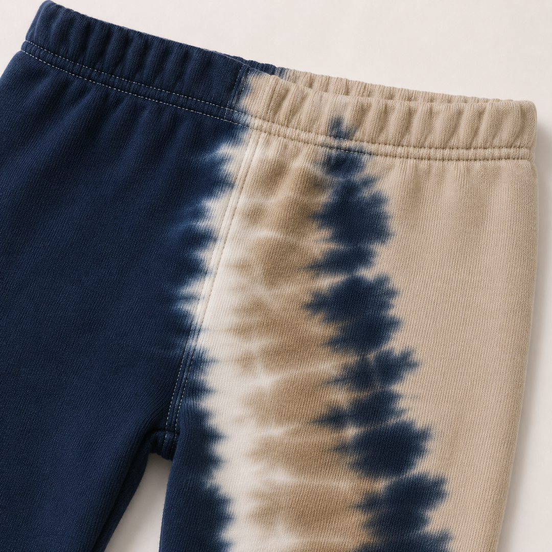 Close-up of a pair of tie-dye sweatpants in navy blue and beige, showing the elastic waistband and fabric texture.