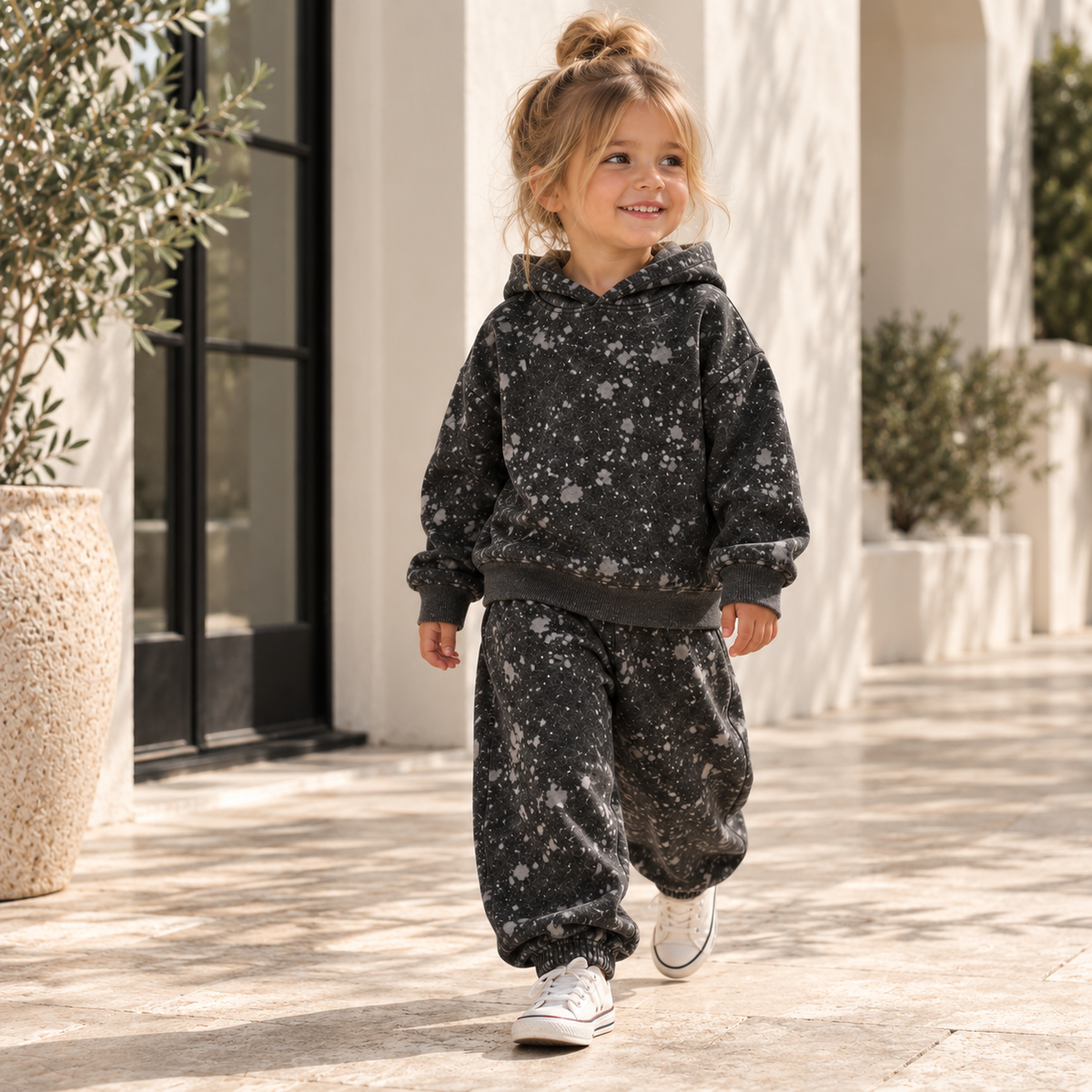 Toddler girl wearing a PAIGELAUREN black splatter hoodie and baggy pant loungewear set in a sunlit California setting.