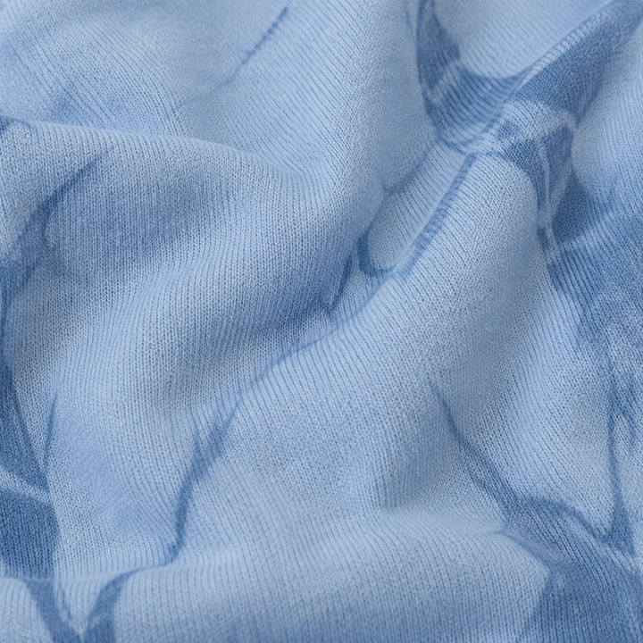 A close-up of light blue knit fabric with a darker blue abstract tie-dye or brushstroke pattern.