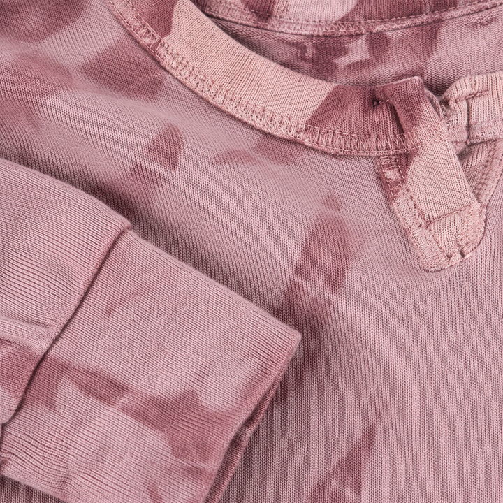 Close-up of a dusty pink long-sleeve top with a tie-dye pattern, showing the ribbed collar and sleeve cuff.