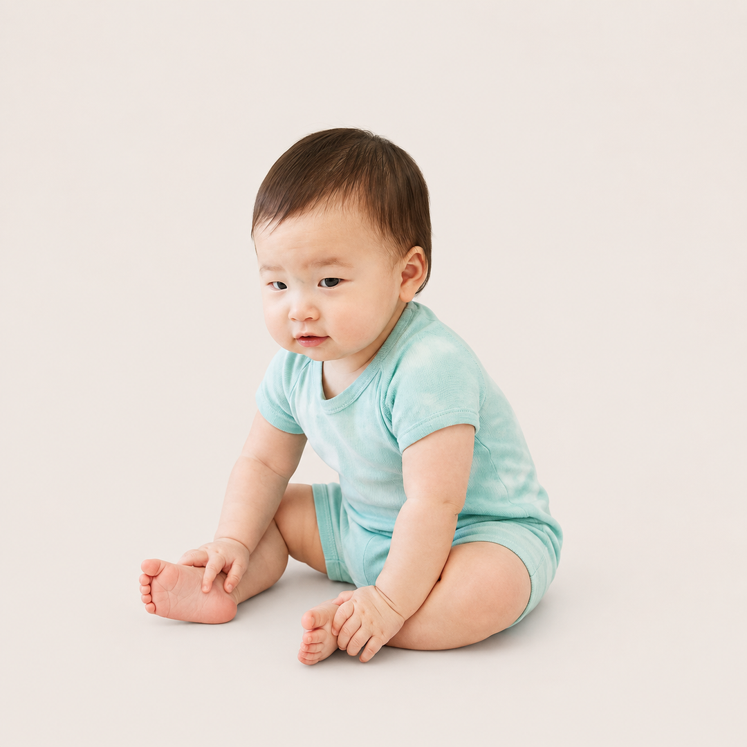 Baby sitting while wearing the PAIGELAUREN Light Green Marble Rib Shortall Onesie